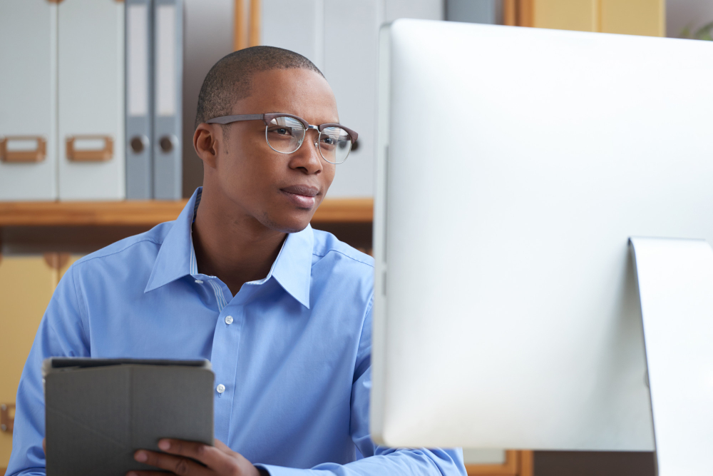 A KYC Analyst at work, wearing blue collar shirt, staring at his desktop.